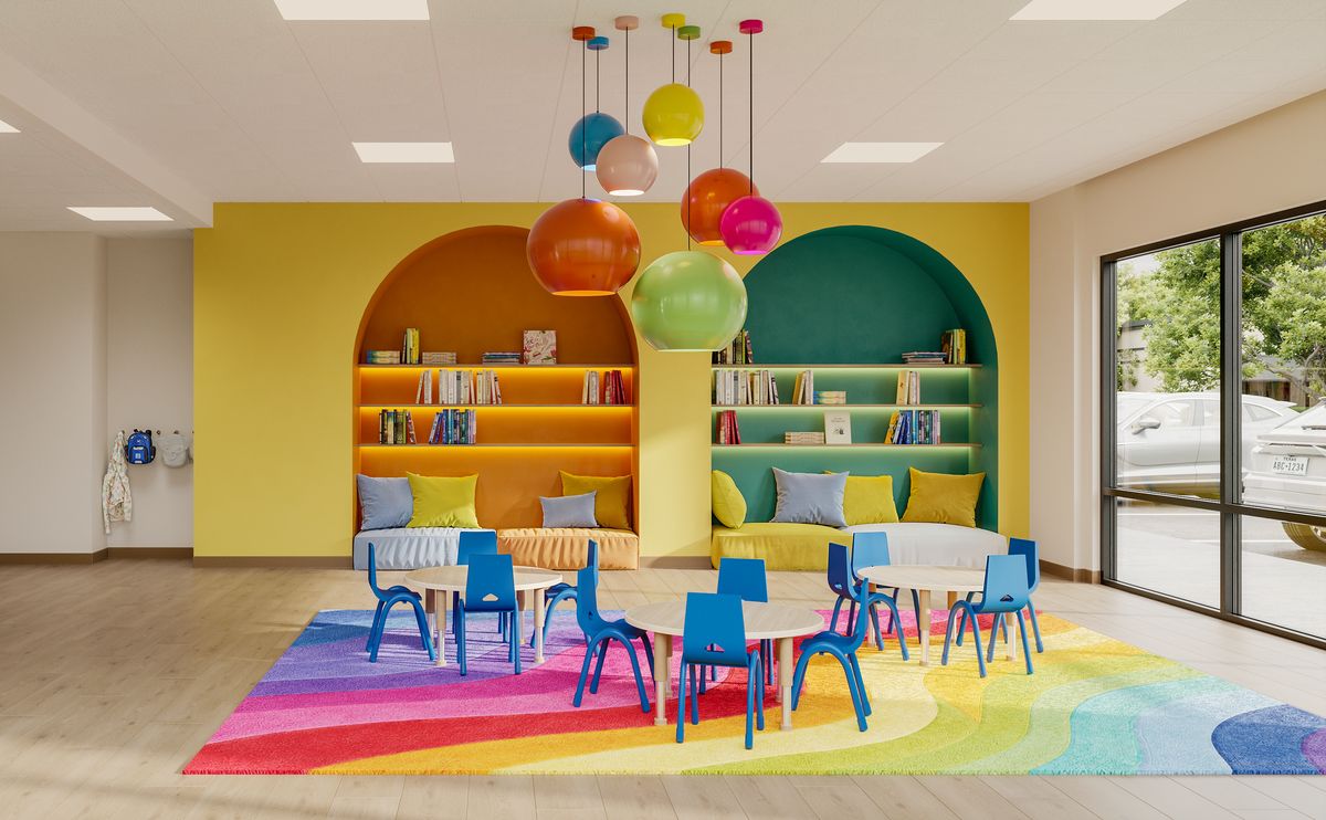 The classroom: a bright yellow wall with orange and green reading nooks, colorful pendant lights, small tables with blue chairs, and a rainbow rug